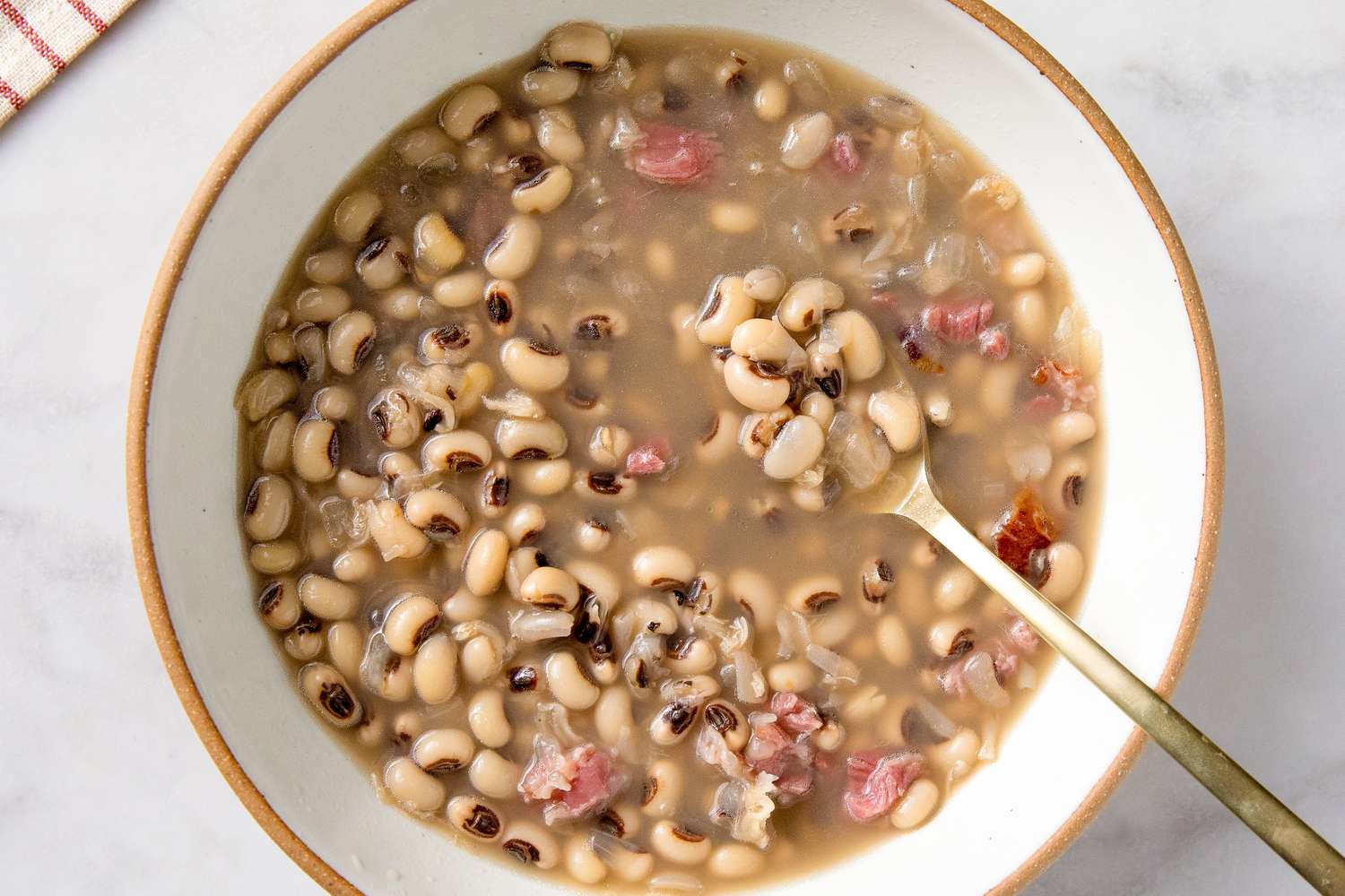 A bowl of cooked blackeyed peas in broth with pieces of meat and a spoon