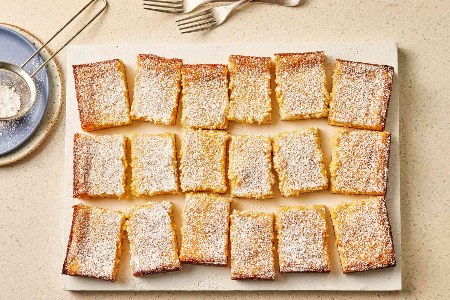 Lemon Gooey Butter Cake slices on a cutting board with powdered sugar in a sifter