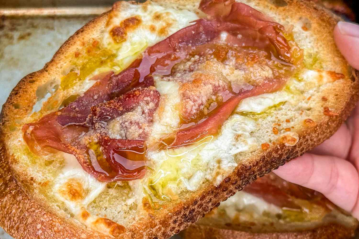 Closeup of fingers holding a toasted slice of ham and cheese toast