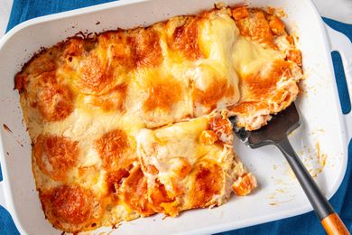 A serving of butternut squash lasagna being scooped from a baking dish with a spatula showing layers of cheese and squash