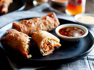 A dark plate with stacked vegetable egg rolls and dipping sauce