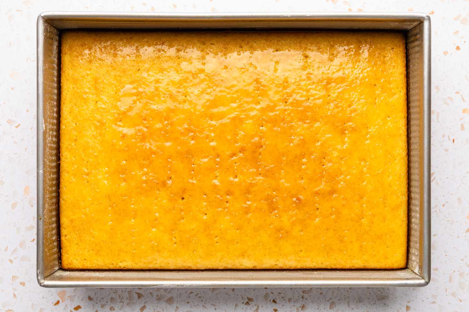 Overhead view of a rectangular cake pan of baked yellow cake on a quartz countertop