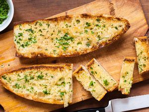 A loaf of garlic bread on a cutting board, partially cut into slices