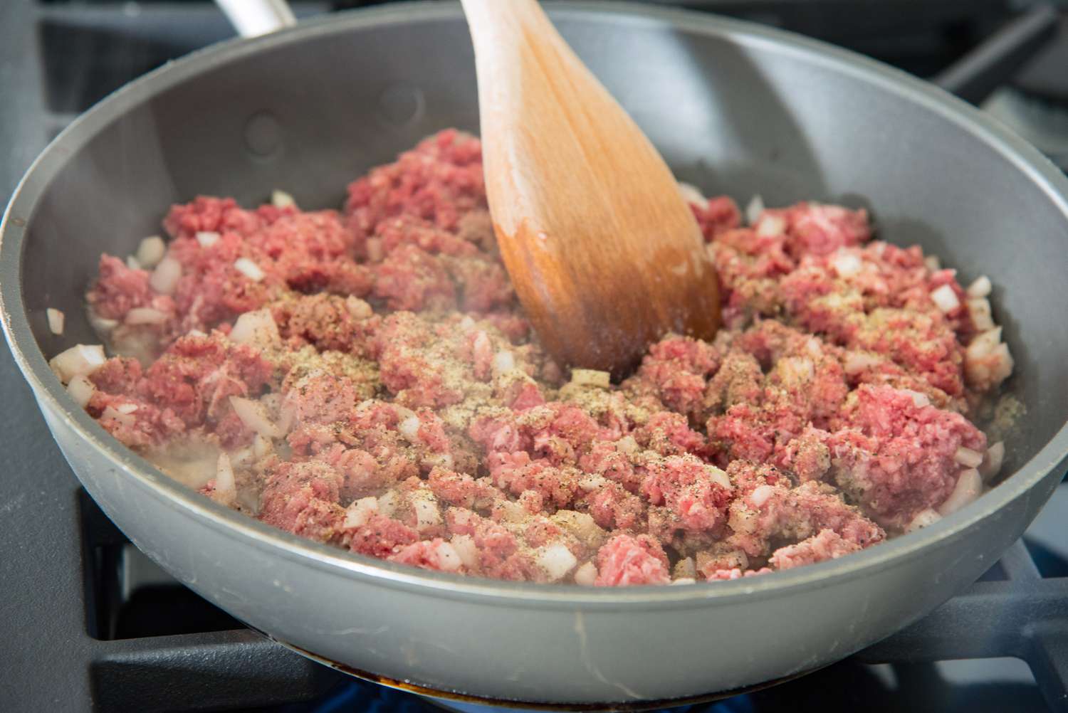 Ground Beef and Onions Stirred in a Skillet as They Cook on a Stove for Cheeseburger Pizza Recipe