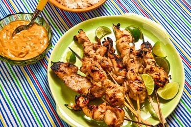 Grilled chicken satay skewers with lime wedges, bowl of peanut sauce and rice served on a plate