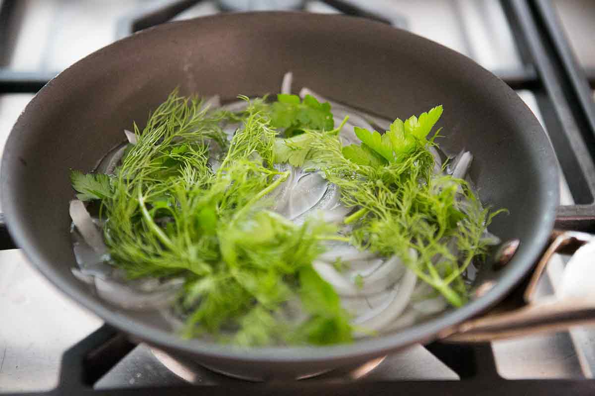 Dill, parsley, and shallot sautéing in a pan on a stove