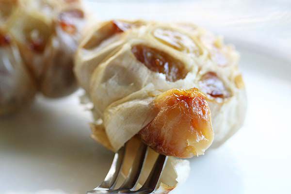 A fork in front of a head of roasted garlic, speaking a clove