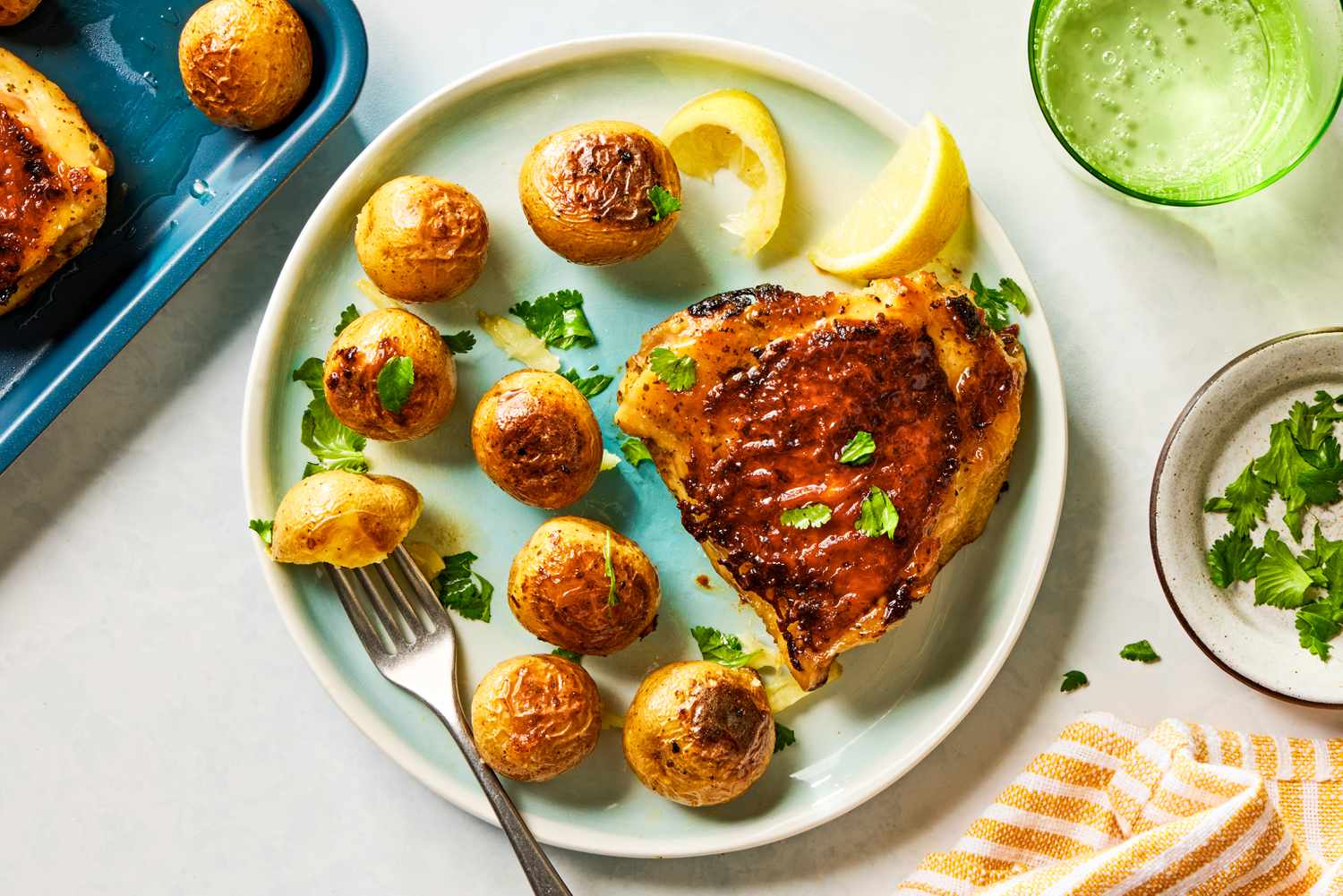 Overhead view of a plate of a roasted chicken thigh, potatoes and lemon slices