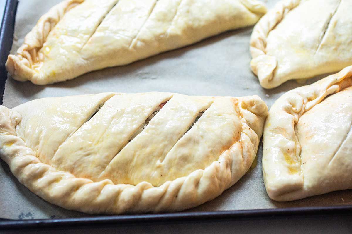 Calzones on a baking sheet with slits in the top.