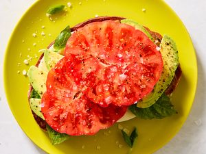 Open-faced sandwich with tomato, avocado, mozzarella, and basil on a yellow plate