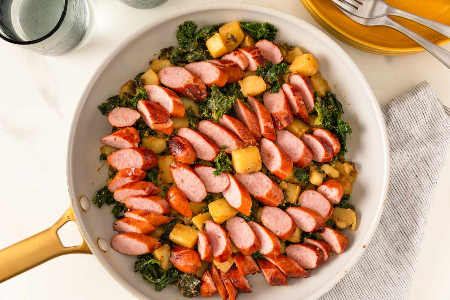 Skillet with sliced sausage potatoes and kale arranged neatly