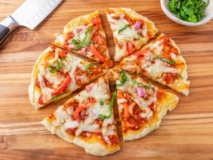 homemade pizza on a wooden counter next to a bowl of chopped basil and a knife