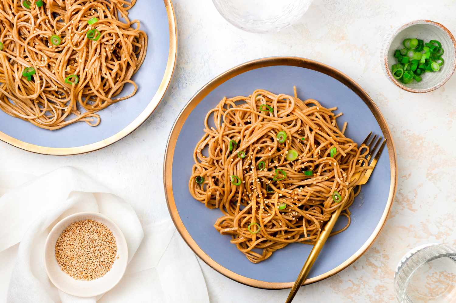 Plates of Sesame Peanut Noodles Next to a Small Bowls of Sesame Seeds and Green Onions