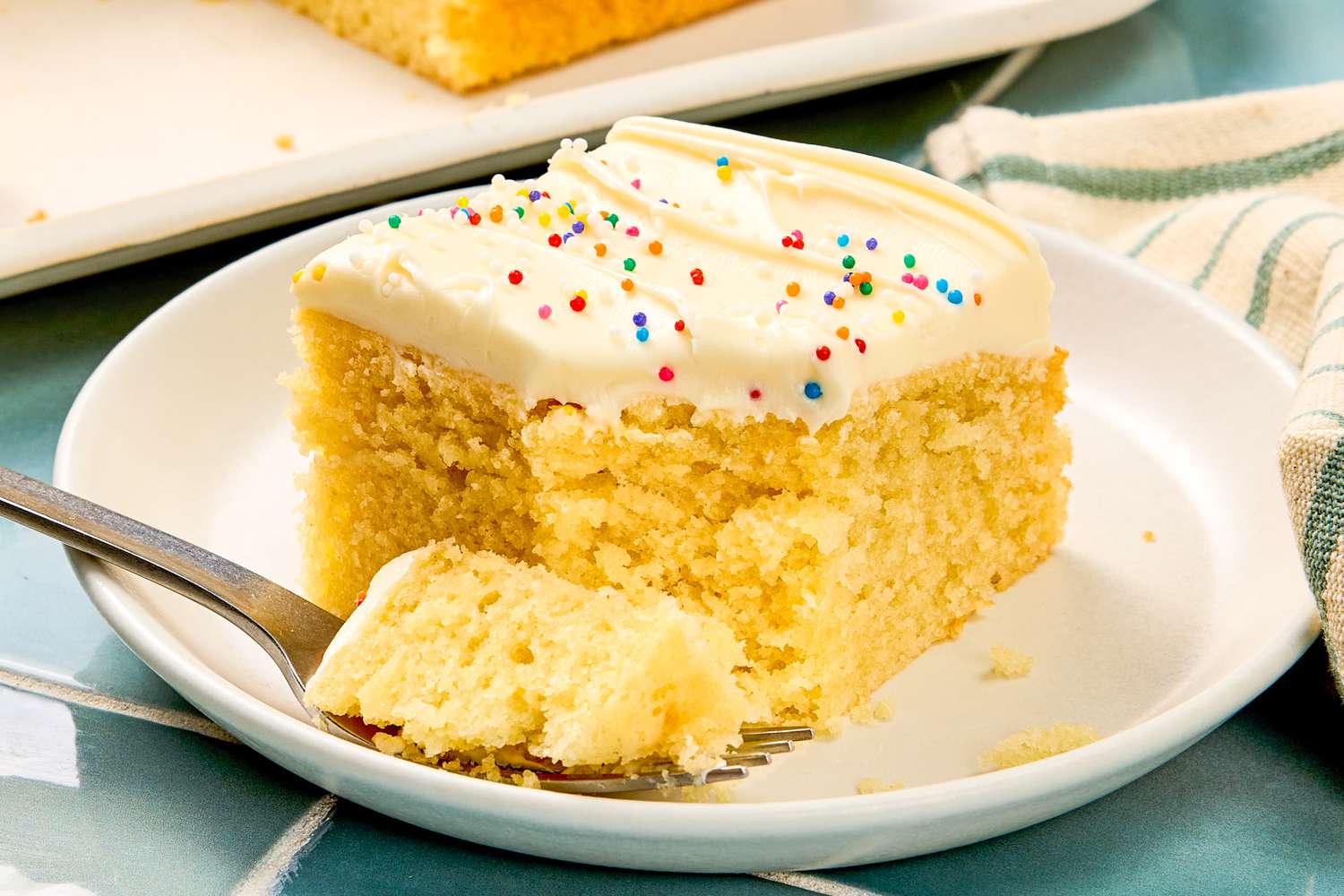 Slice of vanilla cake with frosting and sprinkles on a plate with a fork