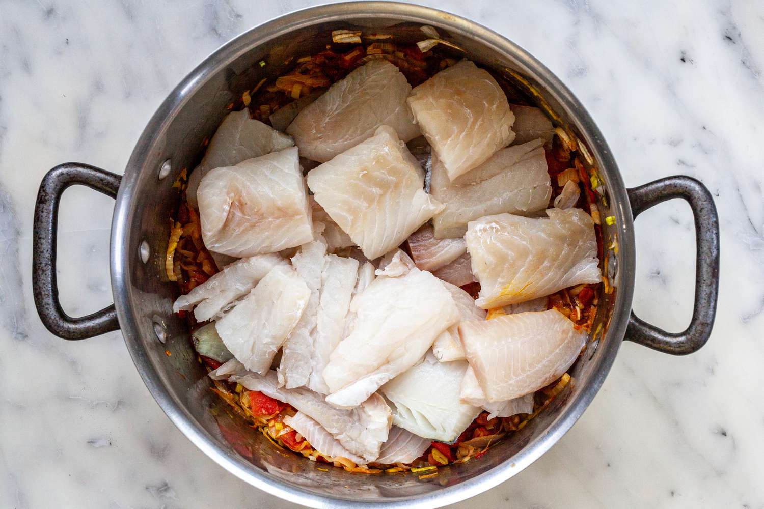 Adding fish to a stock pot for a bouillabaisse recipe.