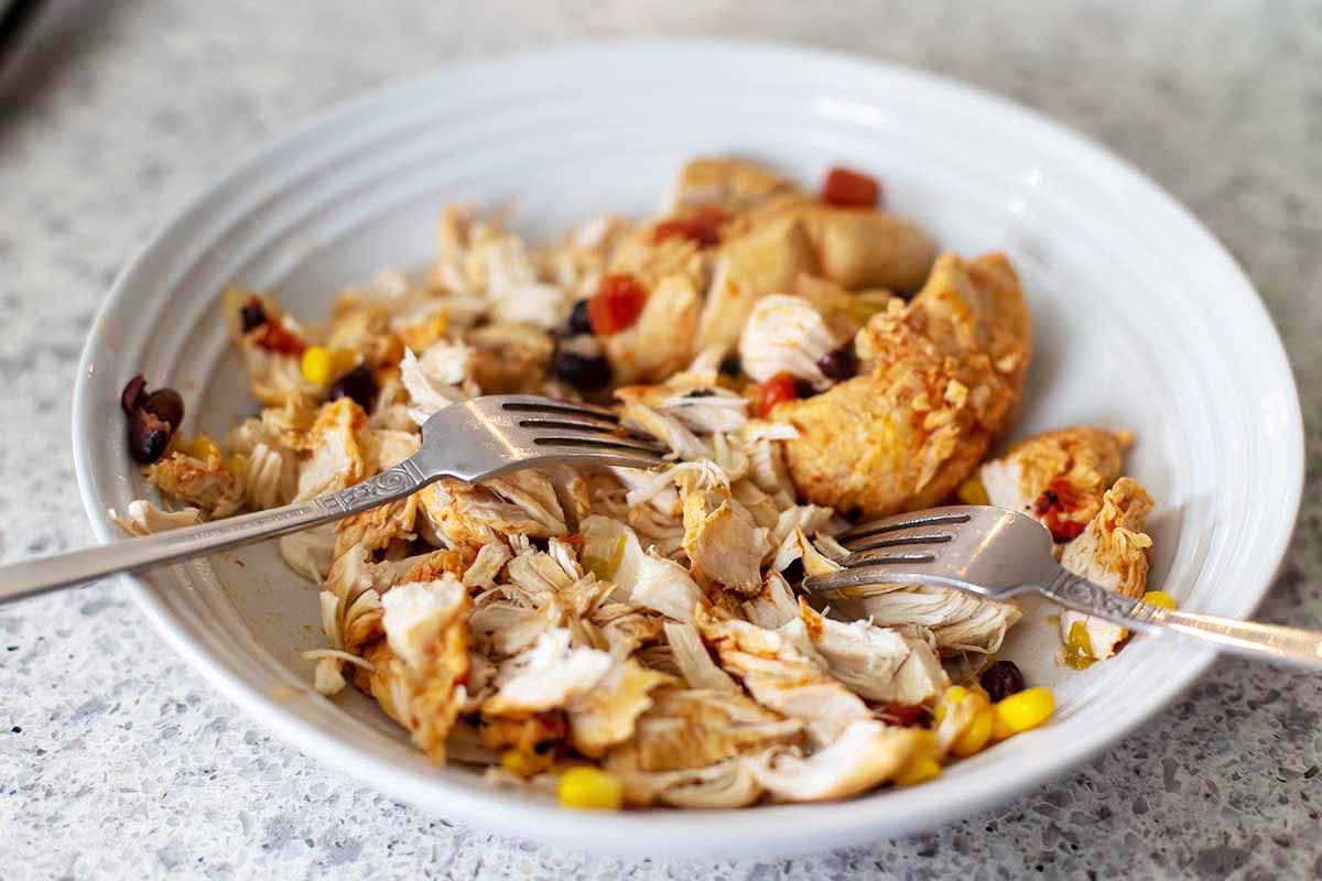 A side view of a shallow bowl with shredded chicken, corn kernals and black beans for easy instant pot chicken tortilla soup.