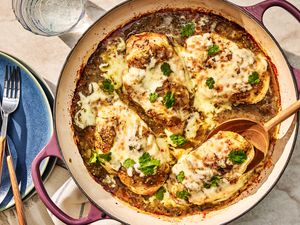salsa verde chicken in a dutch oven at a table setting with a stack of plates with utensils and a glass of water
