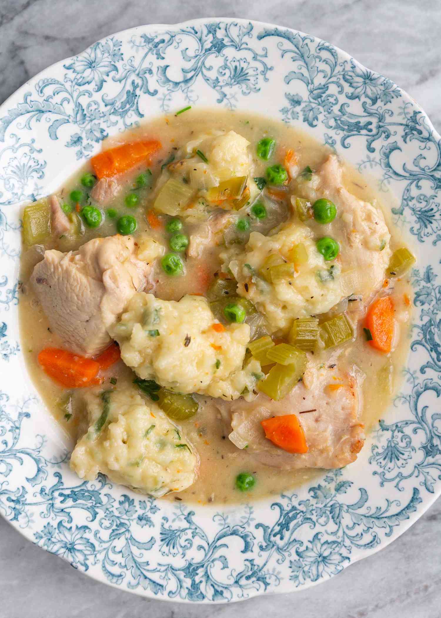 Chicken and dumplings ladled into a china bowl.