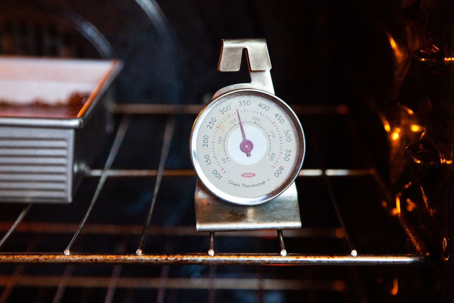 The inside of an oven with an oven thermometer on the baking rack