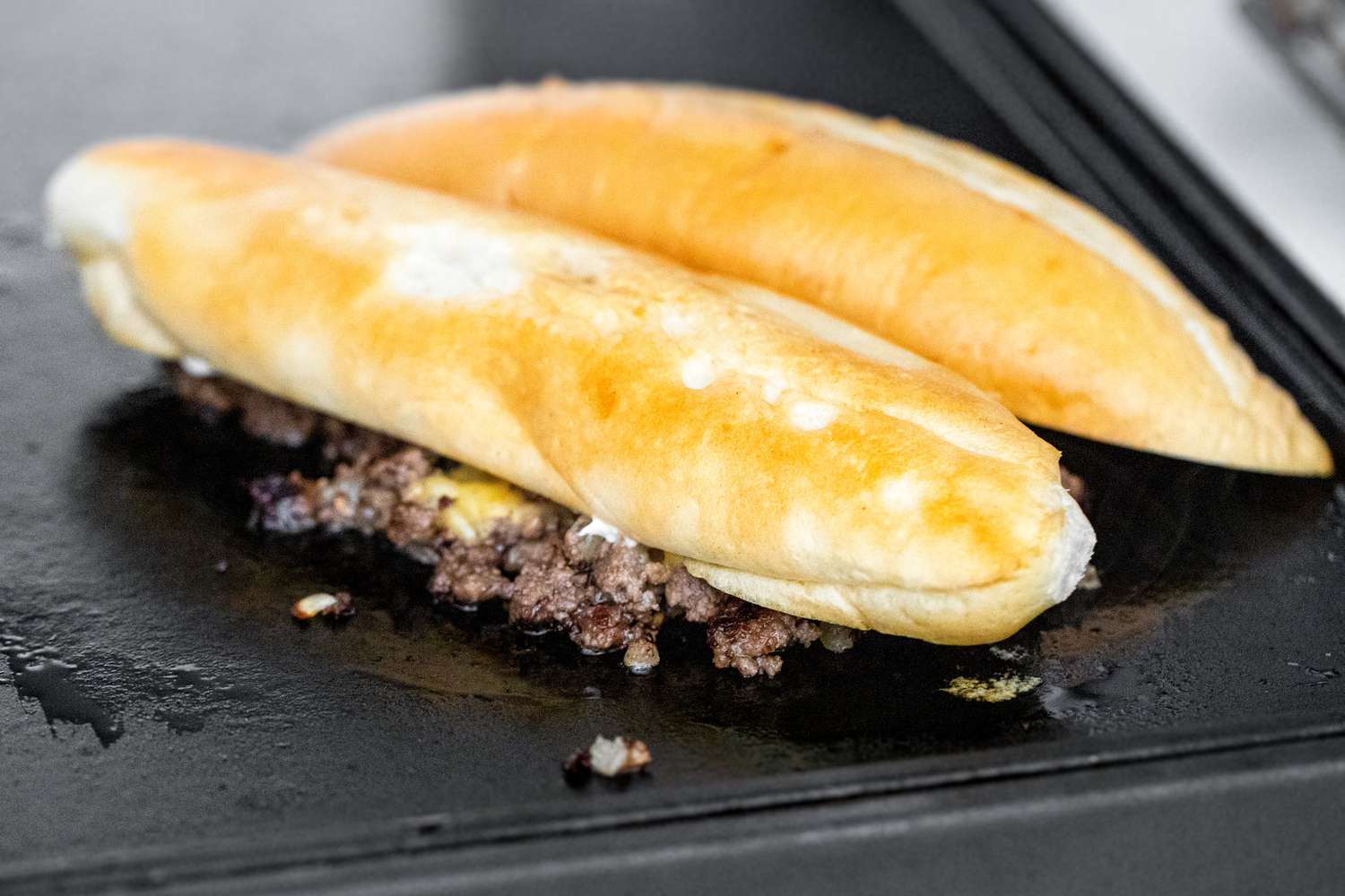 Sliced Hoagie Roll Placed on Top of Chopped Cheese Filling on Griddle 