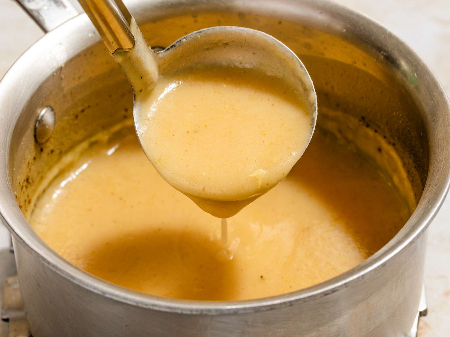 Angled view of a pot of gravy with a ladle removing a serving