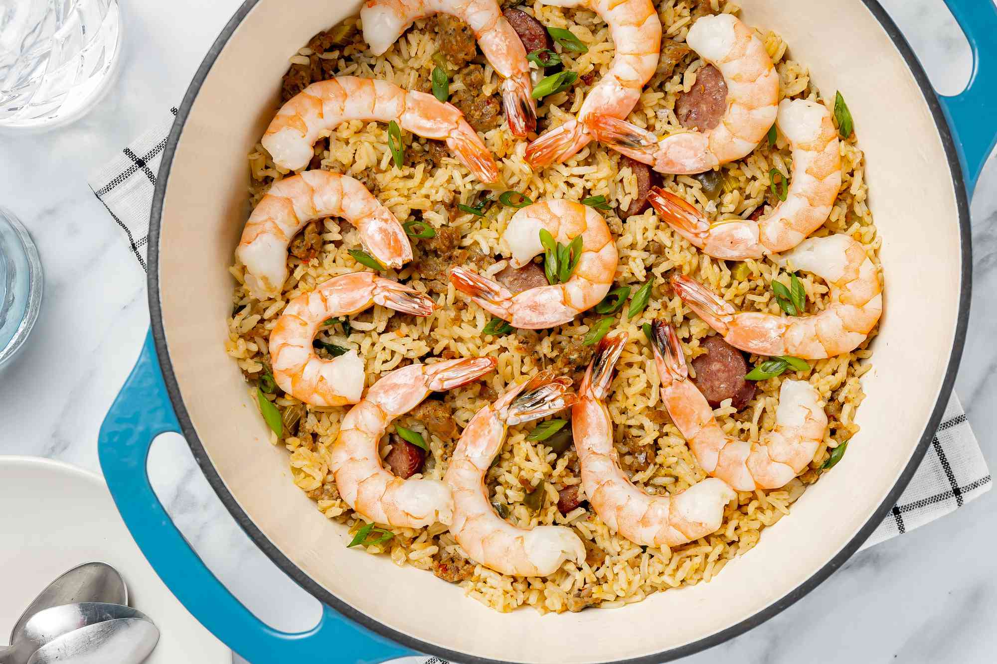 Dirty Rice With Shrimp in a Dutch Oven Surrounded by Glasses of Water and a Plate With Utensils