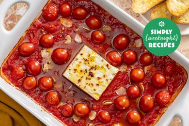 A baked feta dish surrounded by cherry tomatoes in a white baking dish with a Simply Weeknight Recipes logo in the corner
