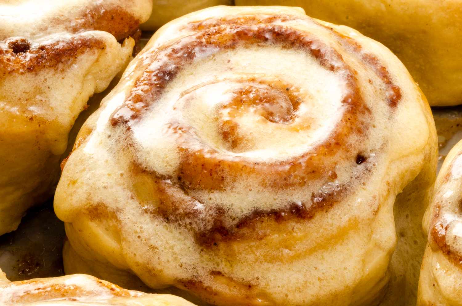 A closeup of a glazed cinnamon roll with visible swirls of cinnamon filling and icing