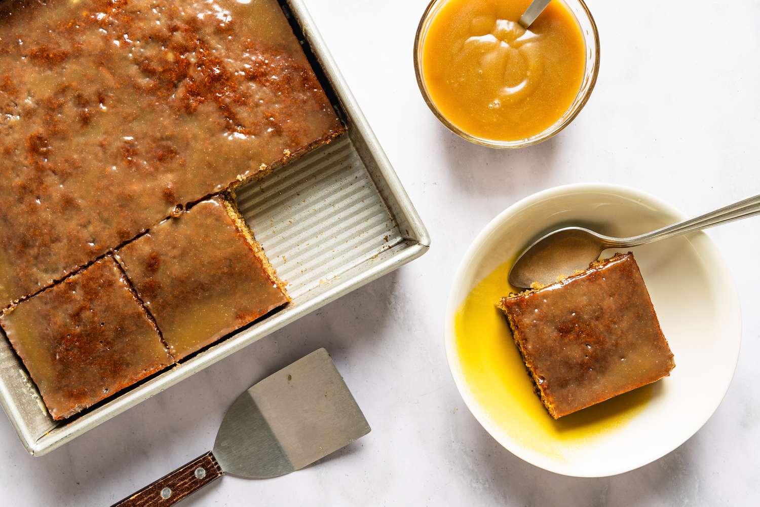 Sticky toffee pudding with a slice served on a plate accompanied by sauce in a small bowl