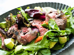 Steak salad made with thinly-sliced pan-seared flank steak on a bed of arugula and lettuce with avocado, pomegranate seeds, and other add-ins