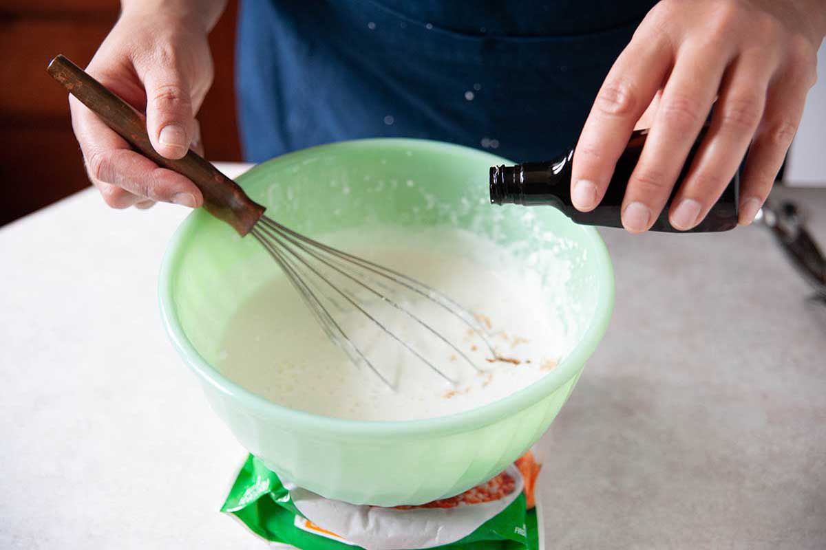 Vanilla being added to the bowl of whipped cream to make homemade whipped cream.