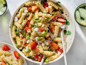 Plate of rotini pasta salad with strawberries feta and greens served on a table with glasses of water