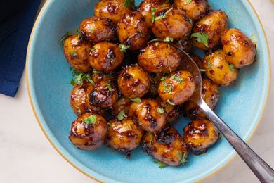 A bowl of Southwestern sticky potatoes coated in a saucy glaze with chopped herbs served with a spoon