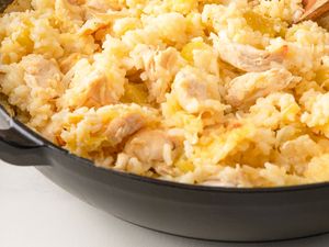 A pan with a dish made of rice and chicken pieces being stirred with a wooden spoon