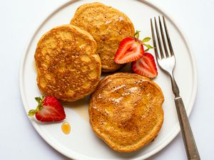 Plate with three almond butter pancakes garnished with strawberries and syrup