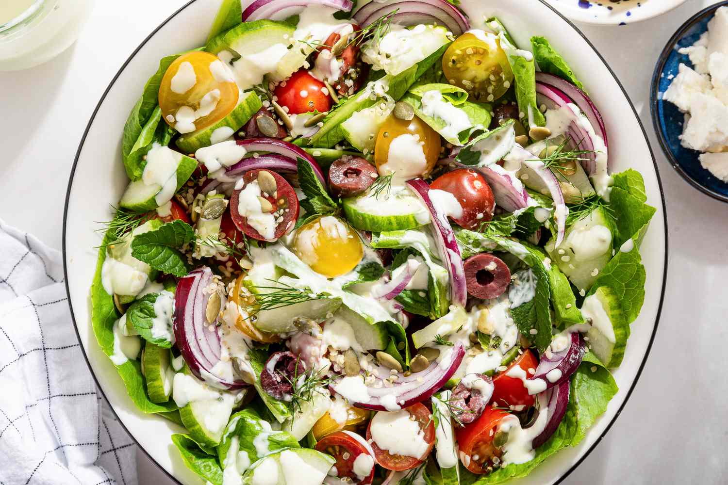 salad with feta dressing at a table setting with a bowl of lemon slices, a bowl with feta pieces, a jar with the rest of the dressing, and a table napkin