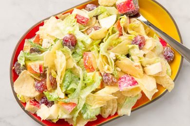 A plate of potato chip salad with grapes and apple slices on a yellow-red platter