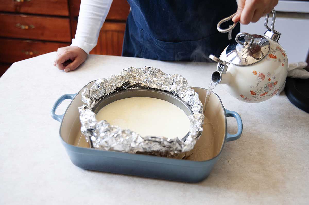 Creme Brulee Cheesecake batter in a springform pan wrapped in foil and set in a roasting tin.