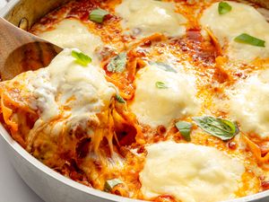 A skillet lasagna being served with a wooden spoon visible layers of pasta sauce and melted cheese