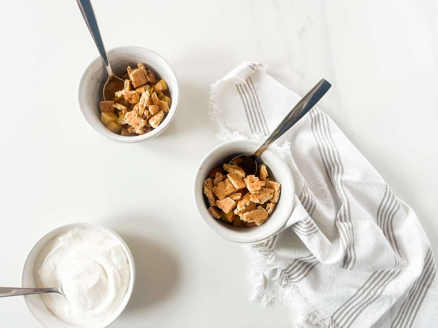 Two servings of a dessert in bowls topped with crust pieces served alongside a bowl of whipped topping and a striped napkin