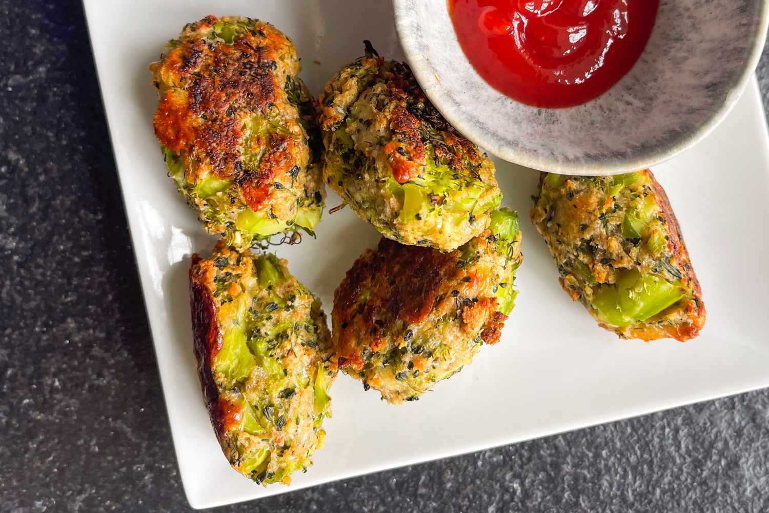 broccoli tots on a plate next to a bowl of ketchup