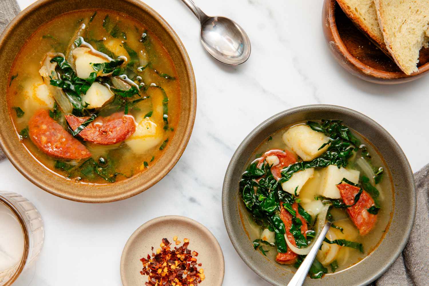 Caldo Verde (Portuguese Kale Soup) in bowls, bread, roasted red pepper and a spoon on the side