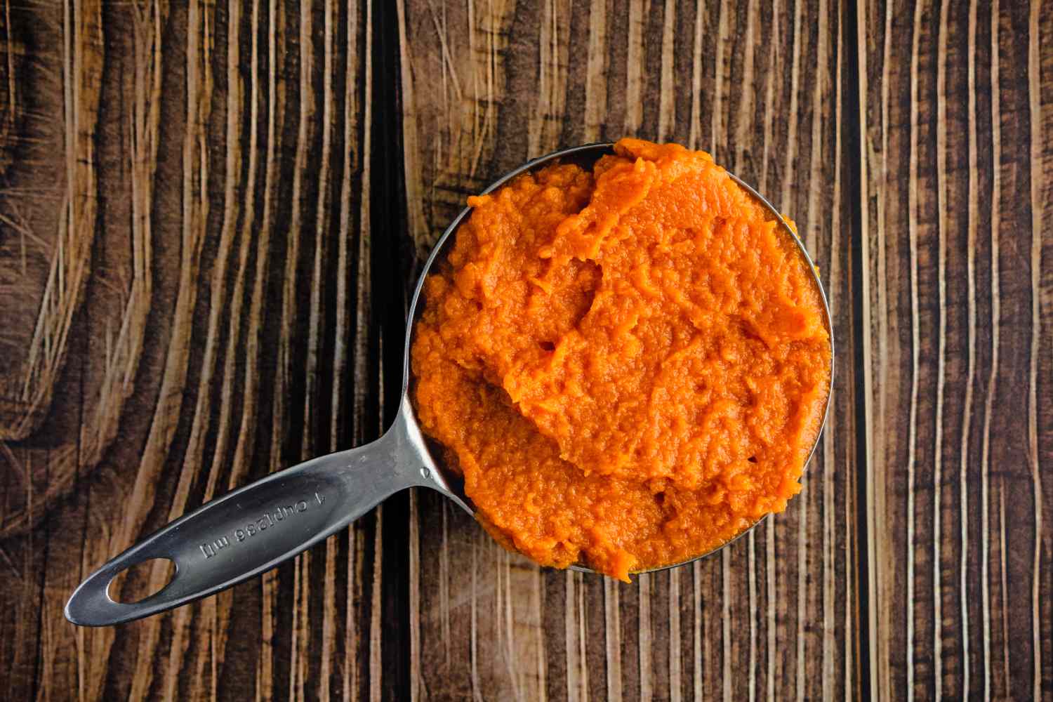 Measuring cup filled with pumpkin puree on a wooden surface