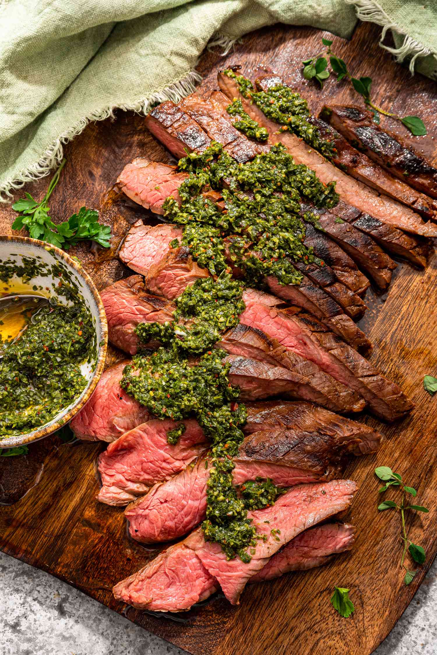 A cutting board with sliced steak and a bowl of chimichurri to the side