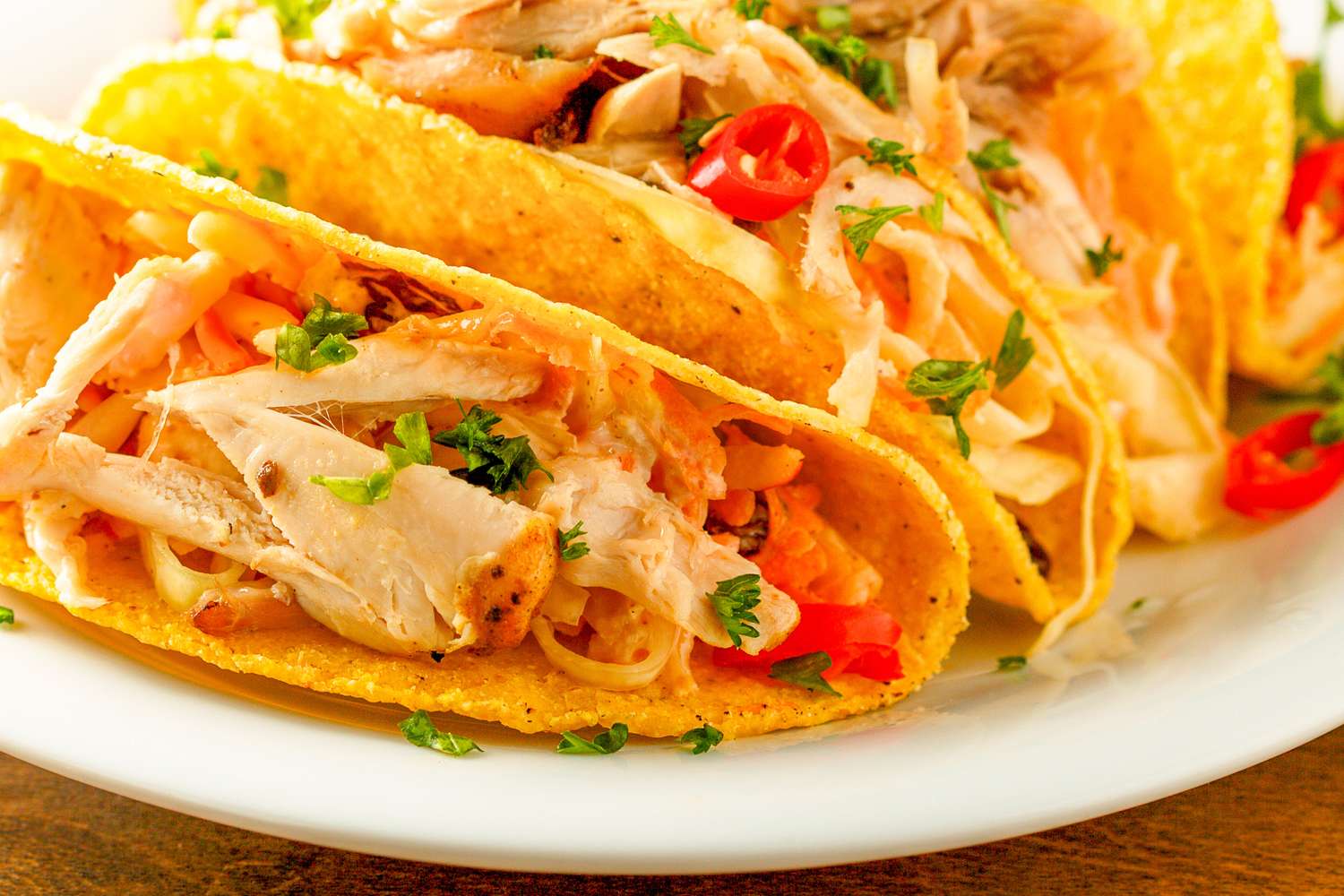 Chicken tacos with shredded rotisserie chicken served in hard taco shells on a plate garnished with parsley and sliced red chilis