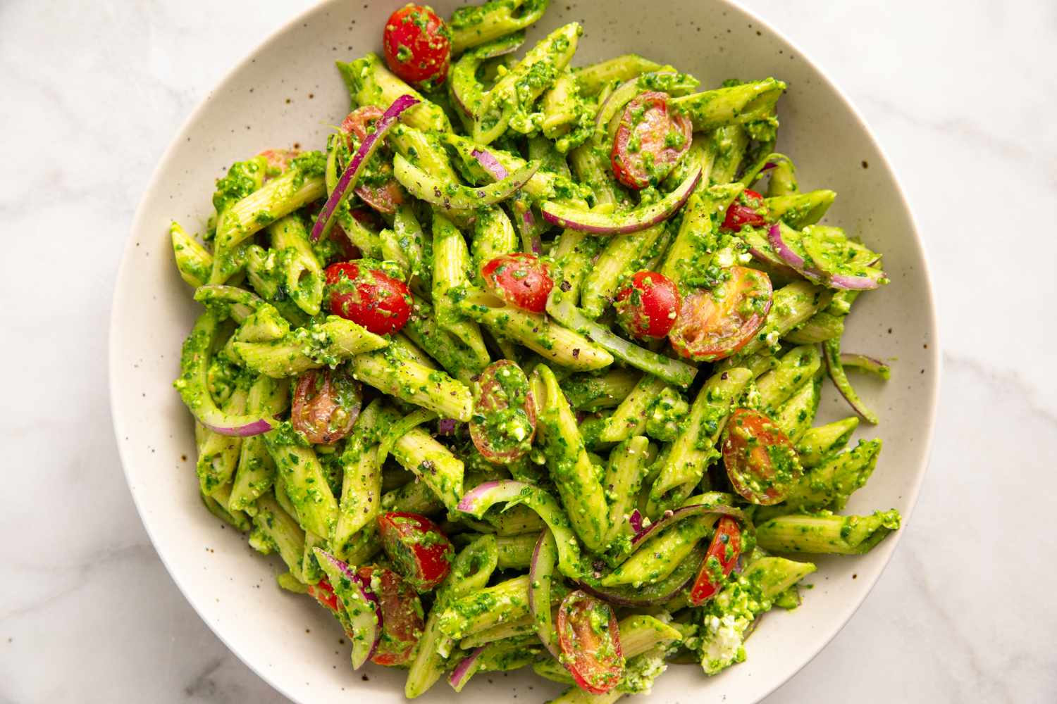 Pasta with cherry tomatoes spinach feta cheese and pesto in a bowl