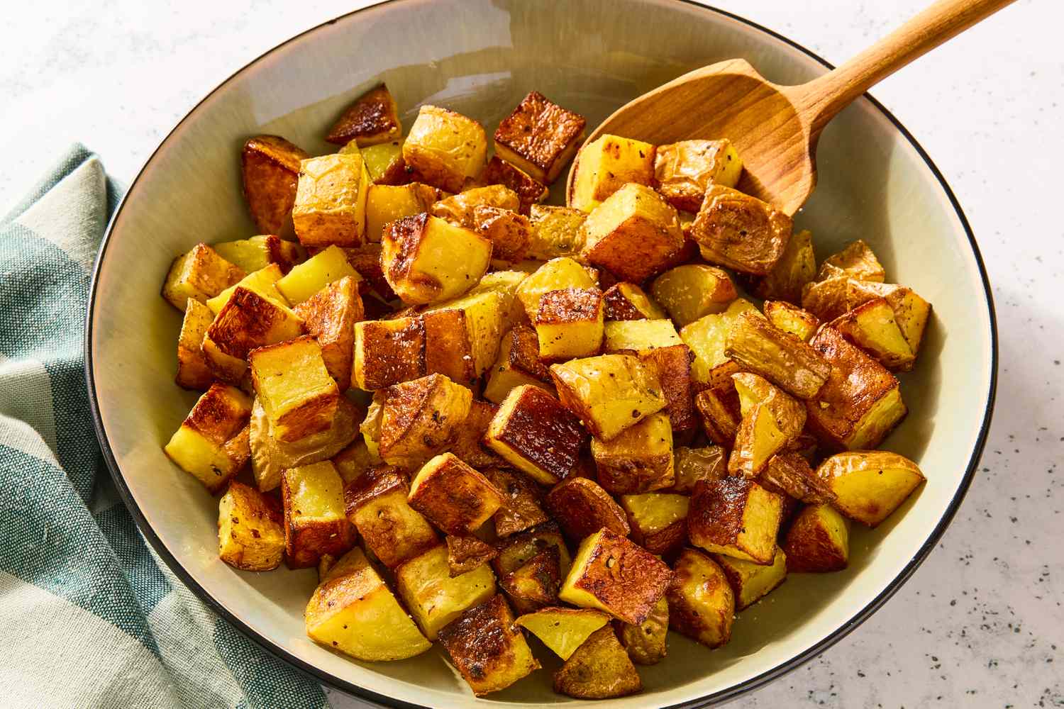 A bowl of roasted potatoes with a wooden serving spoon