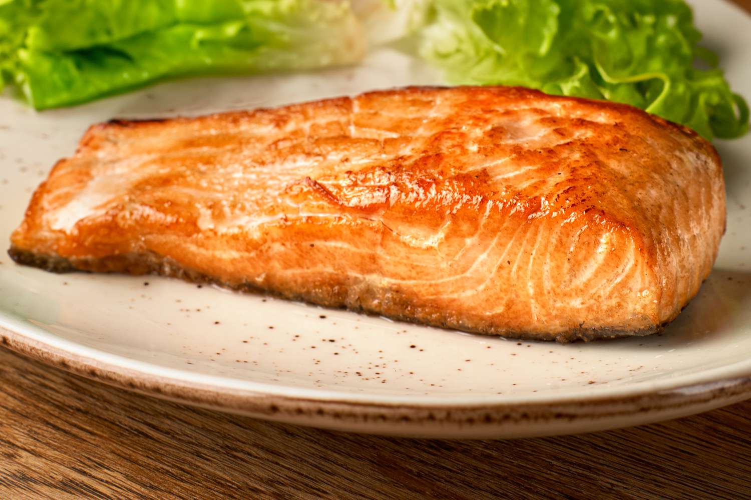 Side view of an oven baked salmon fillet on a pate with lettuce in the background