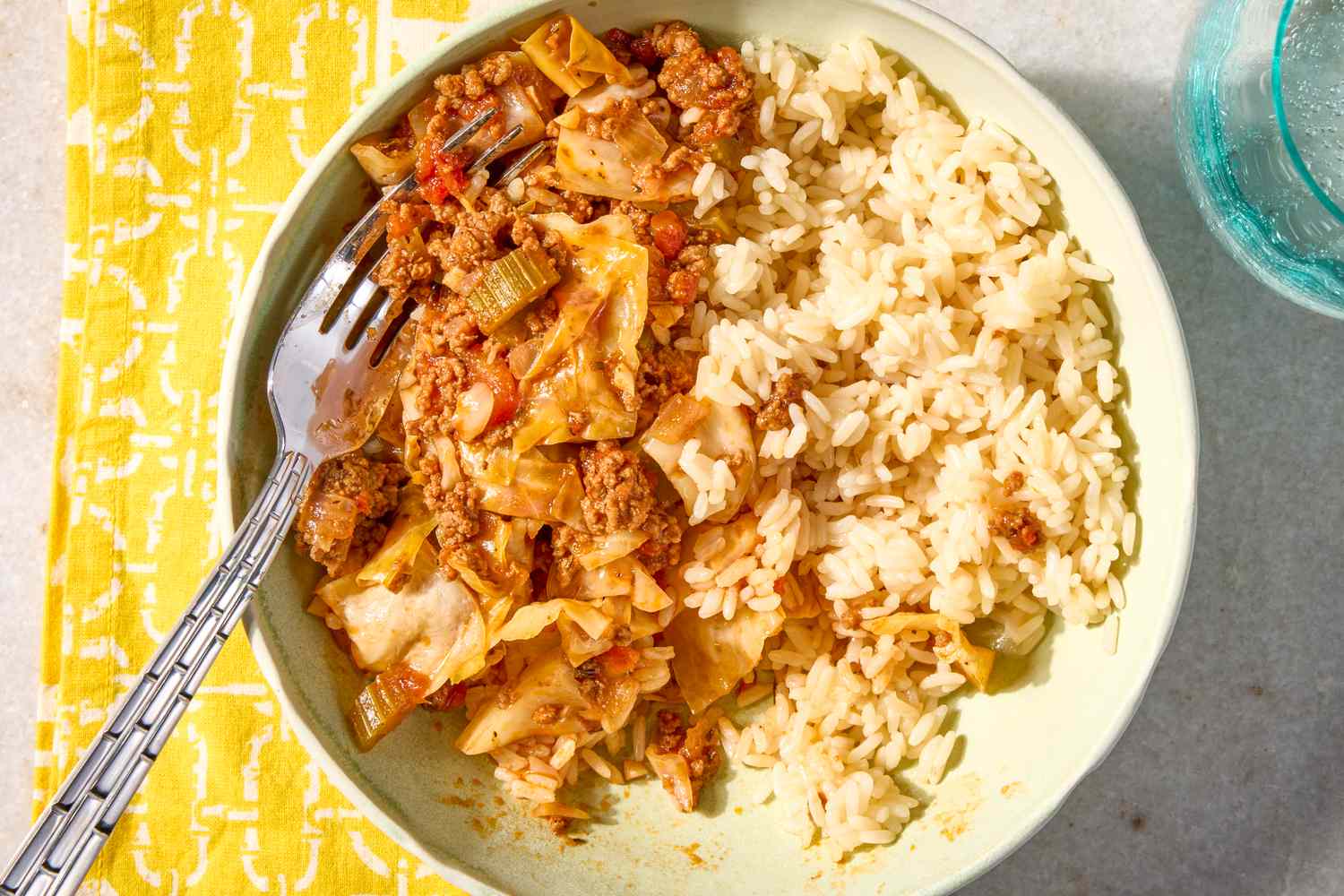 A bowl with a ground beef and cabbage mixture alongside white rice accompanied by a fork