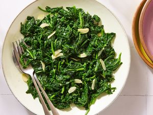 A bowl of sauted spinach garnished with garlic slices two forks resting on the side